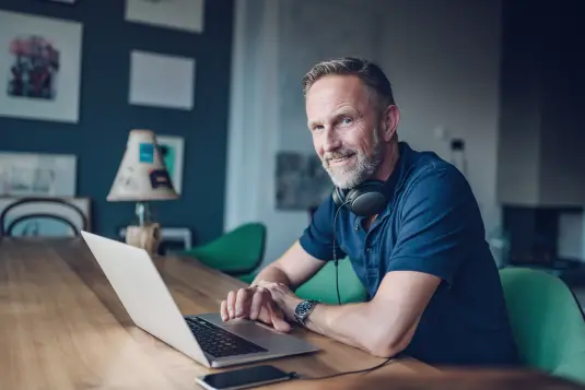 älterer Mann sitzt mit Laptop bei Tisch