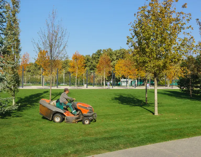 Gemeindemitarbeiter mäht den Rasen im Park