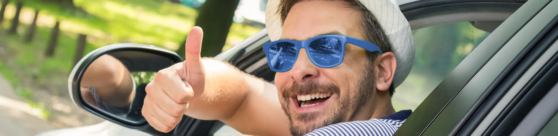Mann im Auto mit Sonnenbrille und zeigt Daumen nach oben
