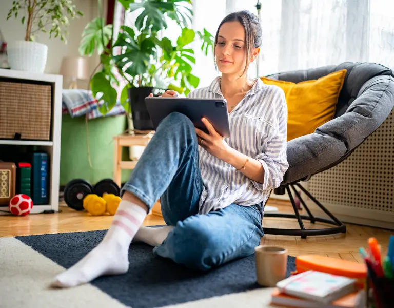 Junge Frau mit Tablet im Wohnzimmer sitzt am Boden