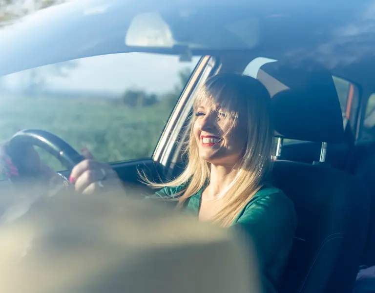 blonde Frau sitzt fröhlich im Auto hinter dem Steuer