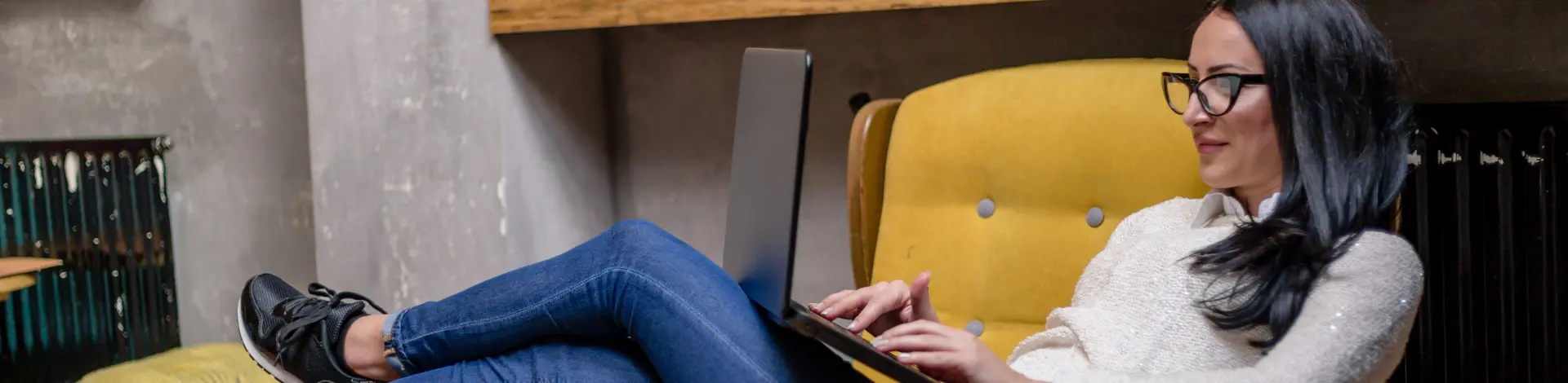 Frau sitzt mit Laptop auf einem Gelben Sessel