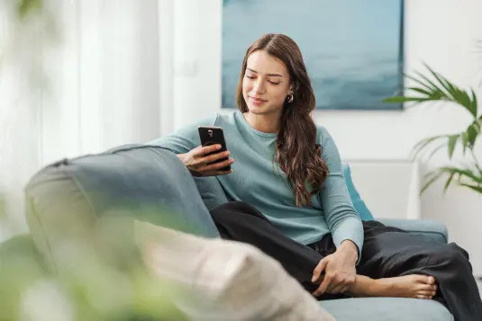 junge Frau sitzend in Wohnung am Handy