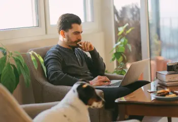 Mann sitzt am Sofa mit Laptop und Hund