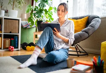 Junge Frau sitzt am Boden und schriebt am Tablet